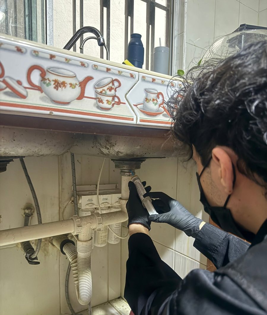 Técnico de FUMITECT aplicando gel en la tubería bajo el fregadero